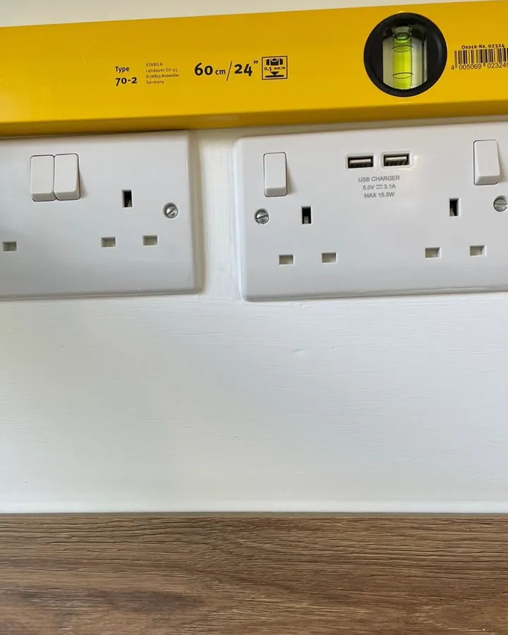 A yellow spirit level held above a row of white sockets that sit at different angles.