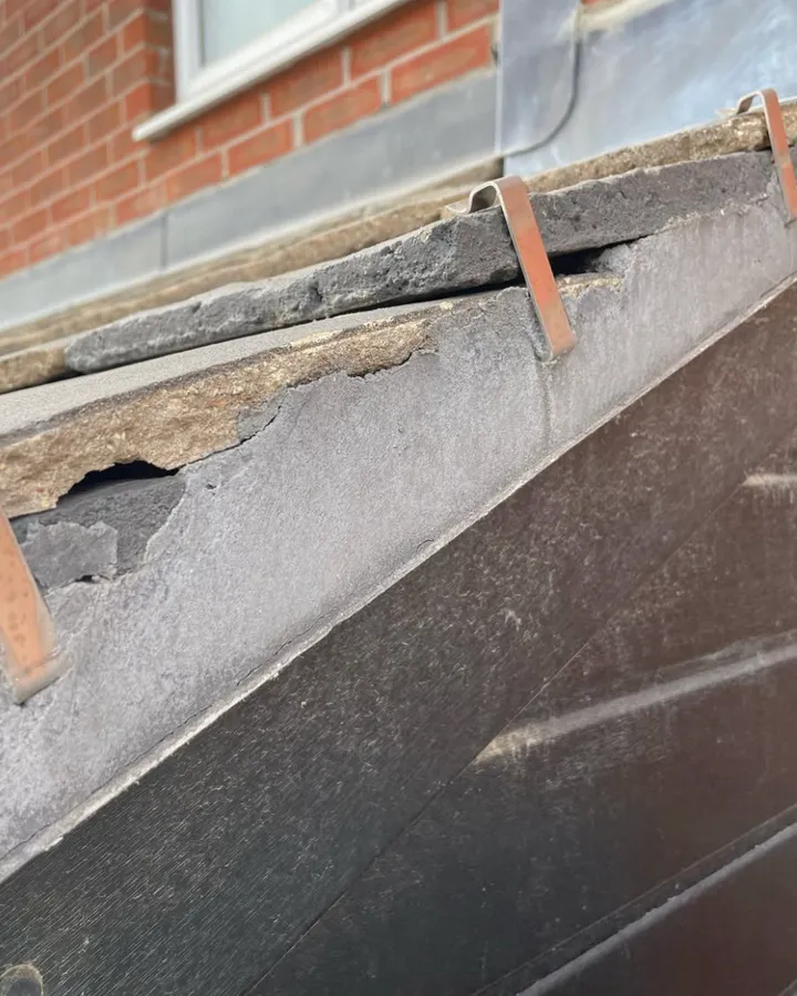 The edge of a slate roof above a dark fascia board, with red brickwork behind.