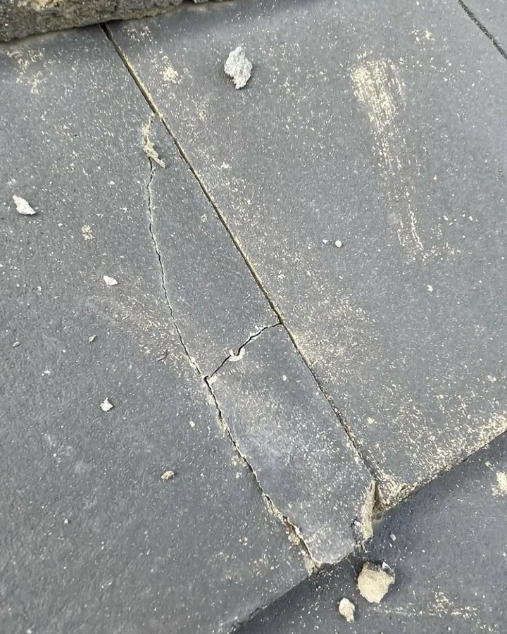 Close view of grey roof slates with dust and small fragments on them.